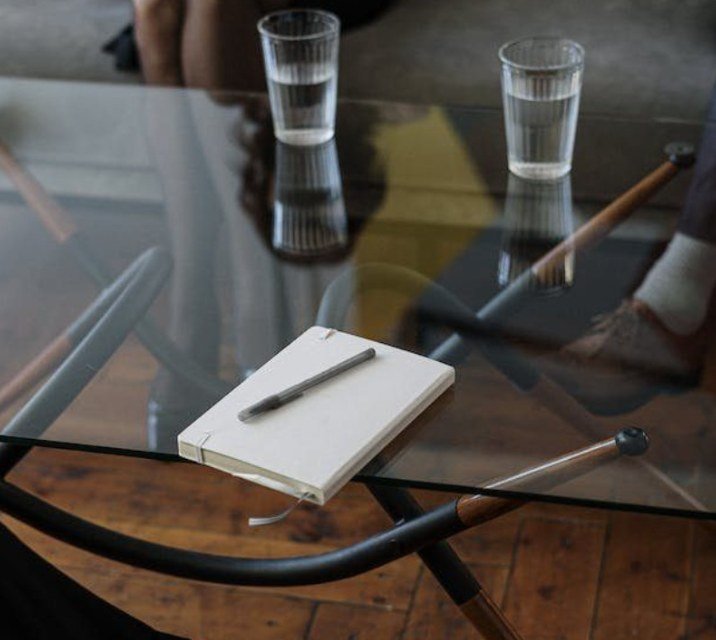 A notebook and pen on a glass table beside two glasses of water