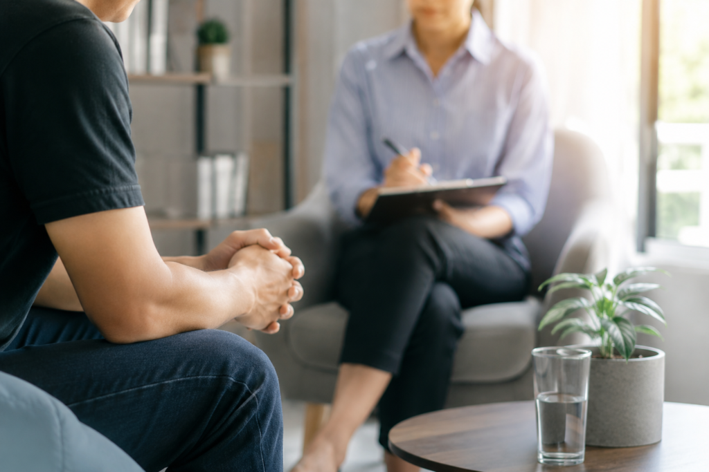 Professional addiction counselling session in Singapore with a client speaking to a counsellor in a calm, modern therapy room. Warm natural lighting, confidential outpatient counselling environment, and supportive mental health and addiction recovery setting.
