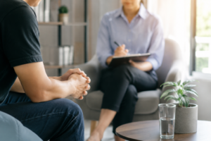 Professional addiction counselling session in Singapore with a client speaking to a counsellor in a calm, modern therapy room. Warm natural lighting, confidential outpatient counselling environment, and supportive mental health and addiction recovery setting.